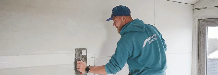 Person verspachtelt eine Wand mit einem Spachtel.